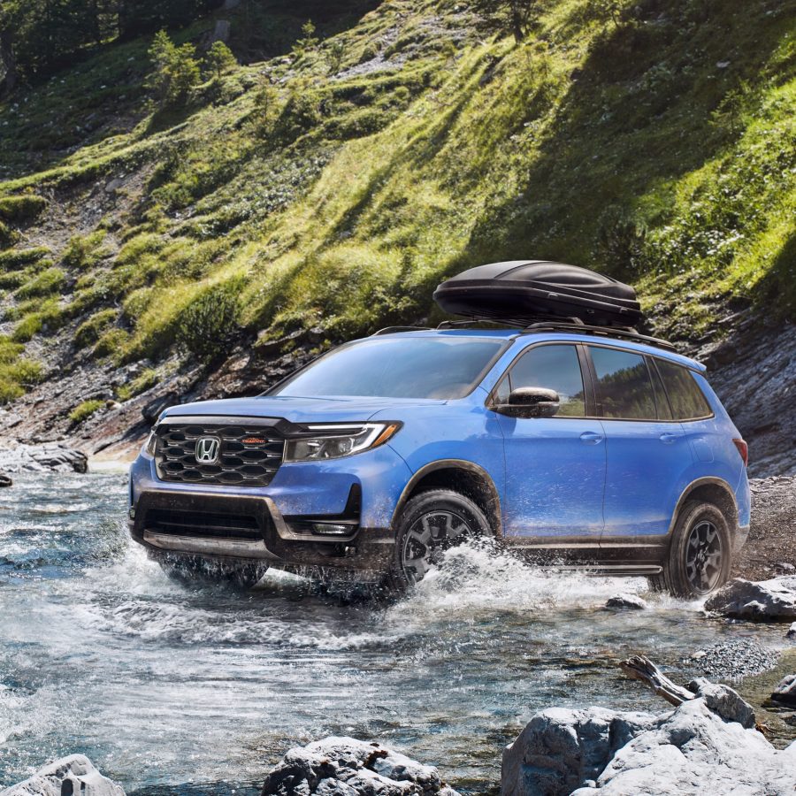 Three-quater view of a 2024 blue Honda Passport Trailsport crossing a river